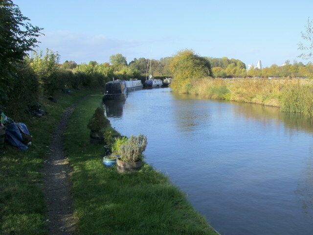 A narrow waterway with boats, a grassy path, and trees.