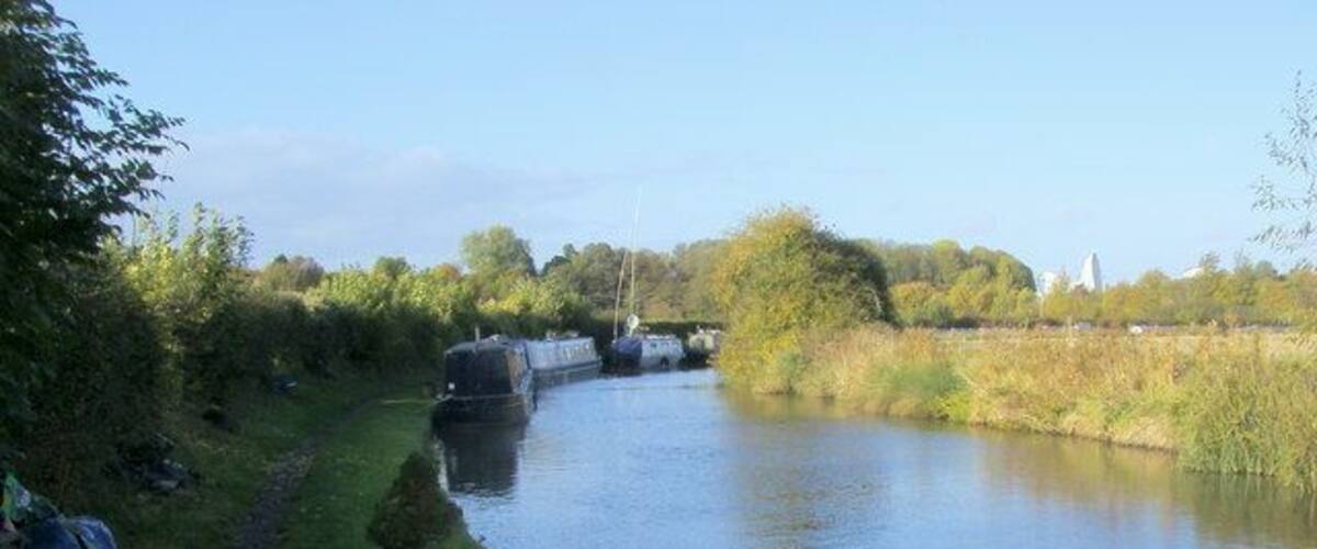 A narrow waterway with boats, a grassy path, and trees.