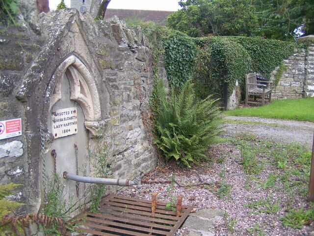 A stone wall with a plaque, a wooden bench, and a fern.
