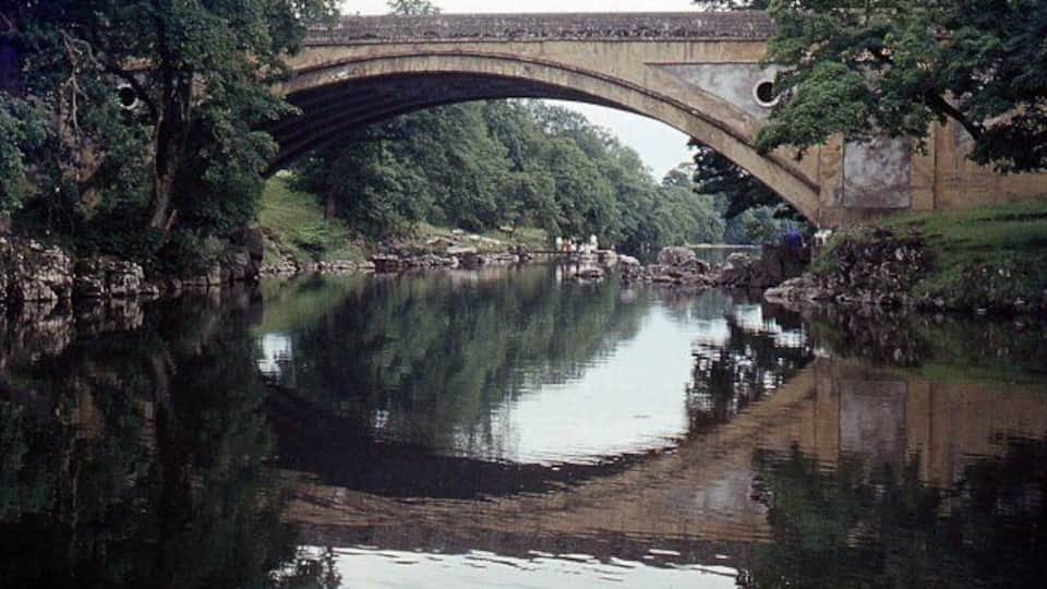 A stone bridge over a calm river with trees reflecting on the water.