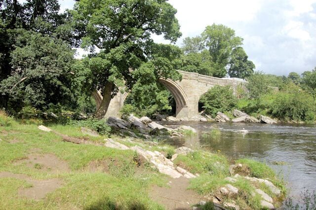 A stone bridge over a river, surrounded by trees and greenery.