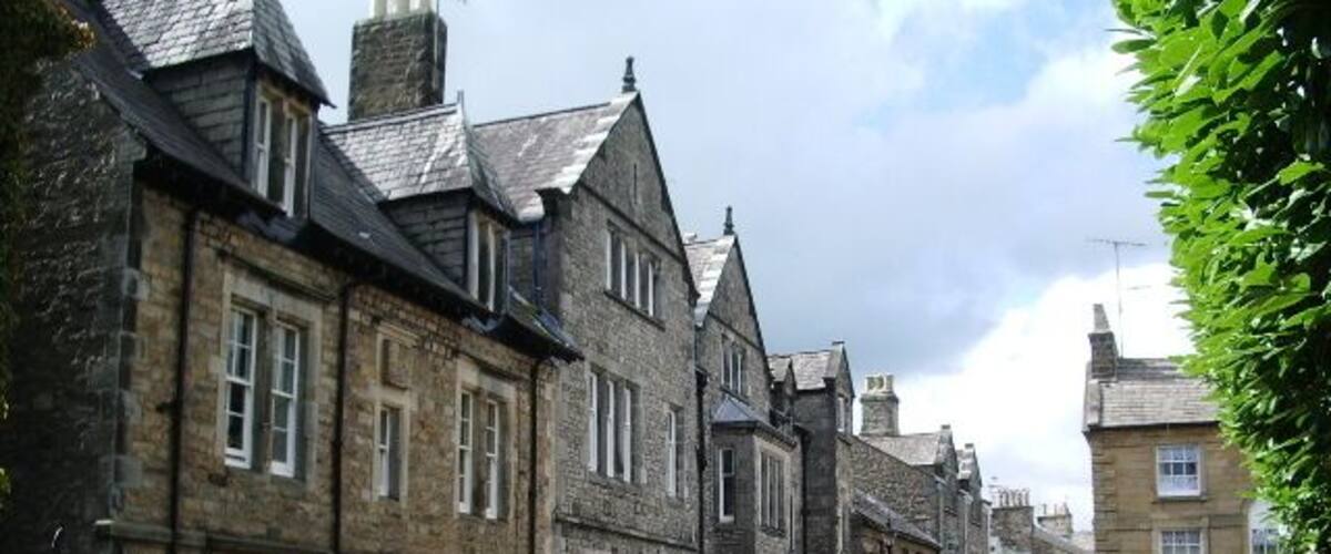 A street lined with historic stone buildings, a clear sky, and parked cars.