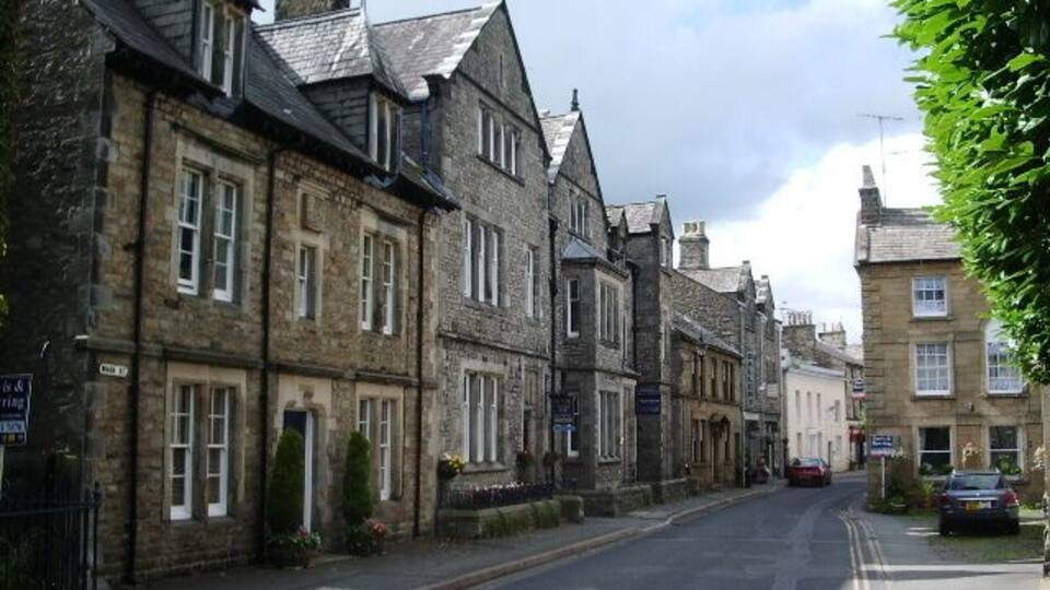 A street lined with historic stone buildings, a clear sky, and parked cars.