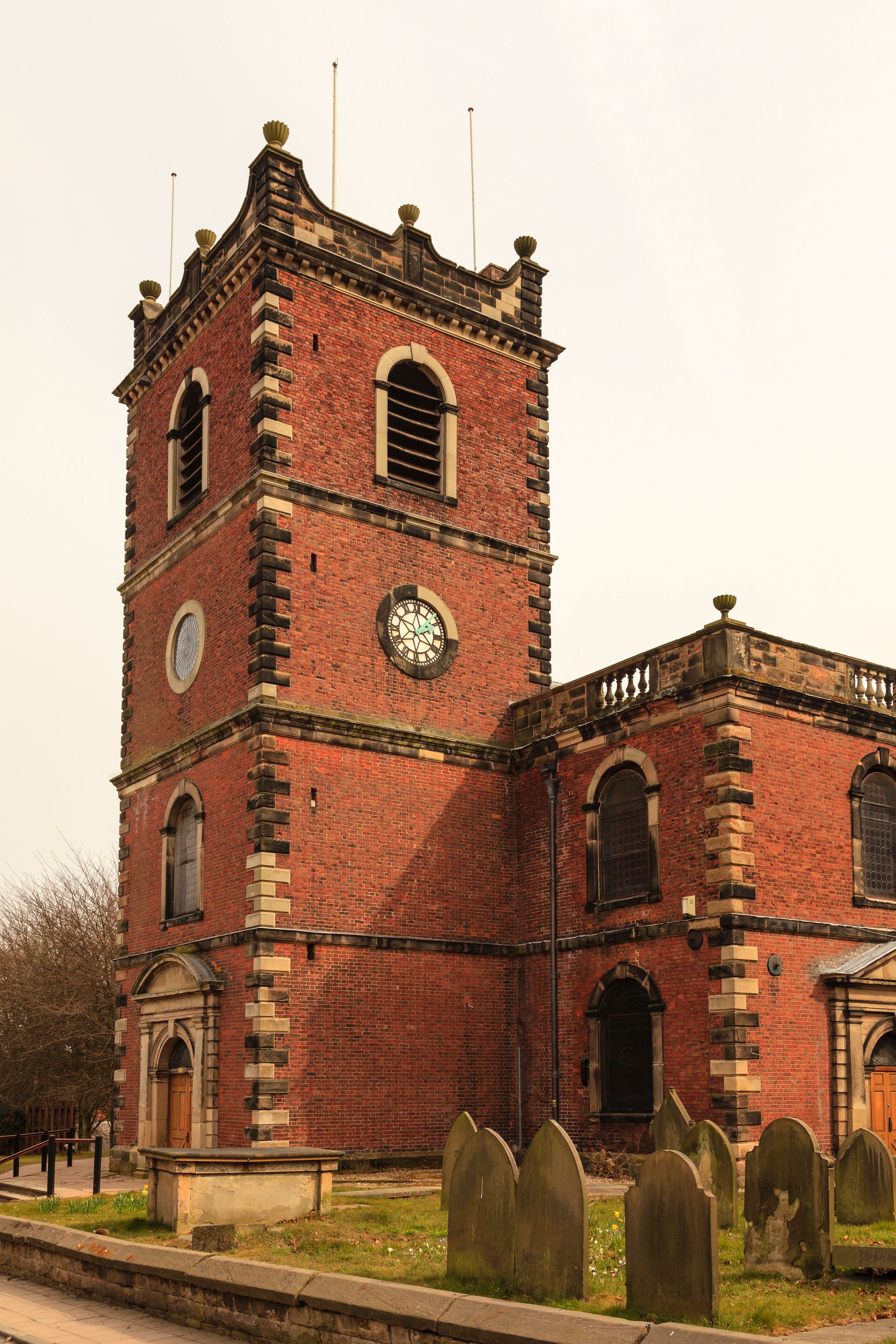 Eine rote Backsteinkirche mit einem Kirchturm, Rundbogenfenstern und einem Friedhof mit Grabsteinen.