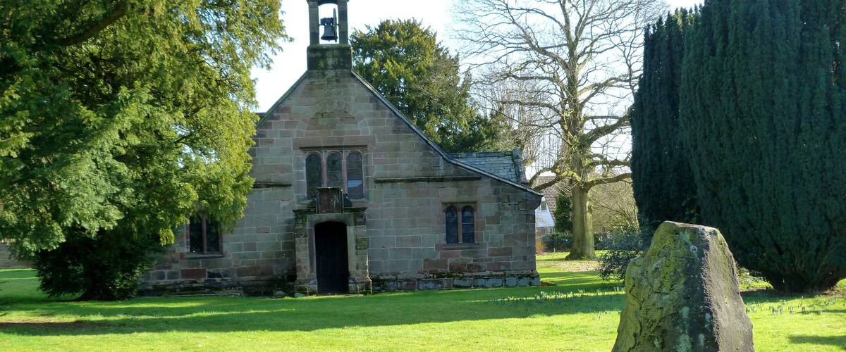 A stone church with a bell tower, surrounded by a well-maintained lawn and a large tree.