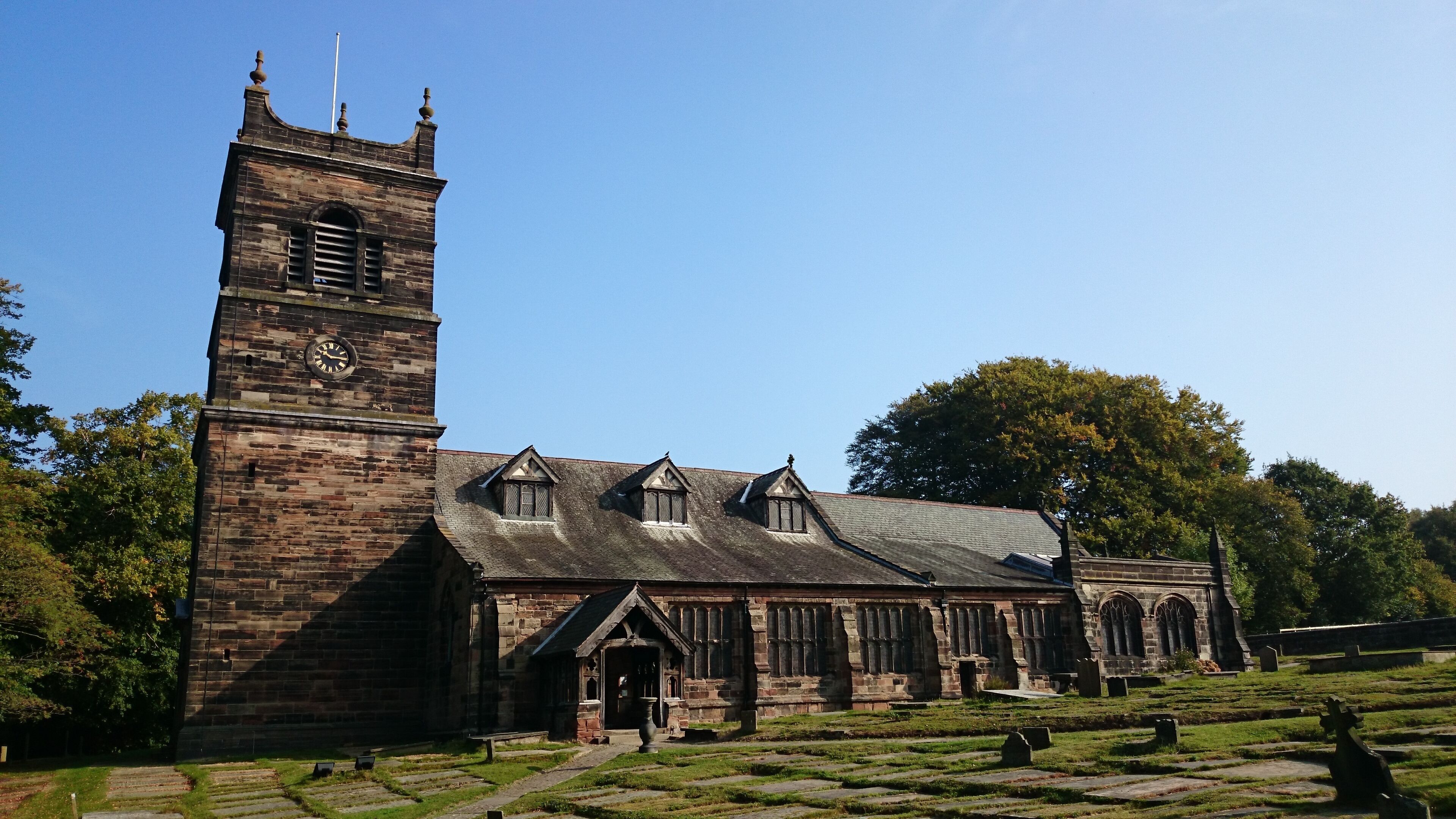 A historic church with a tall clock tower, a steeple, and a cemetery with headstones.