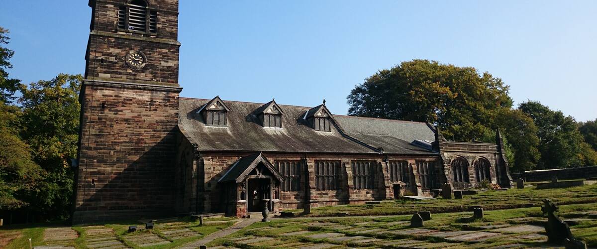 A historic church with a tall clock tower, a steeple, and a cemetery with headstones.