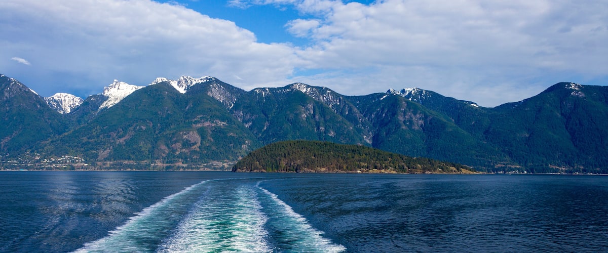 A boat's wake on a calm lake with mountains in the background.