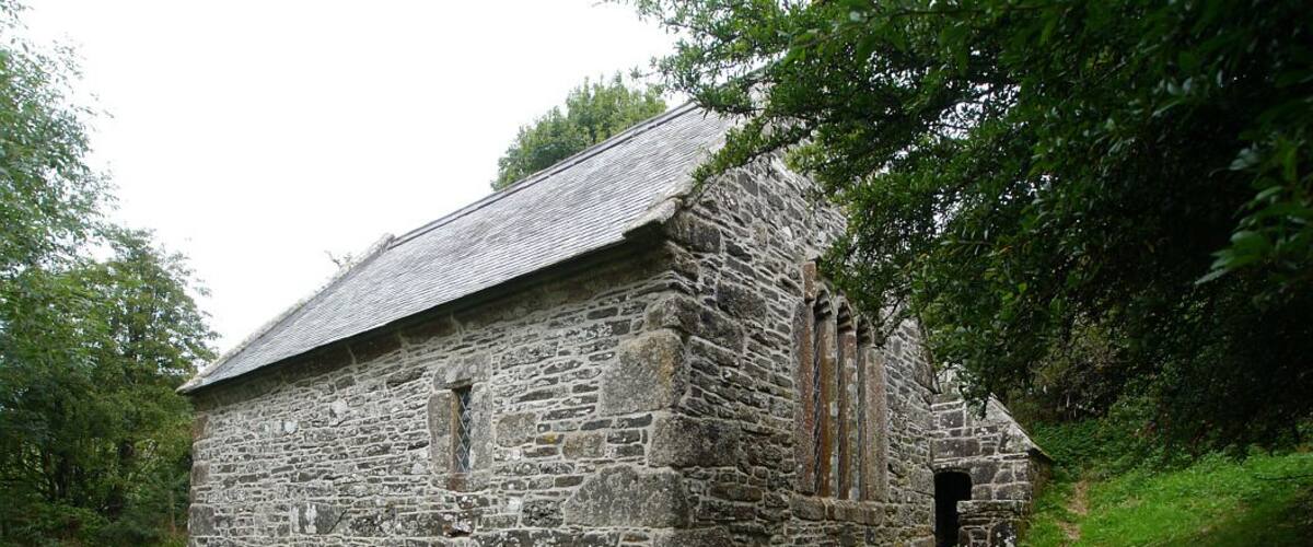 A stone church with a sloped roof, surrounded by lush greenery.