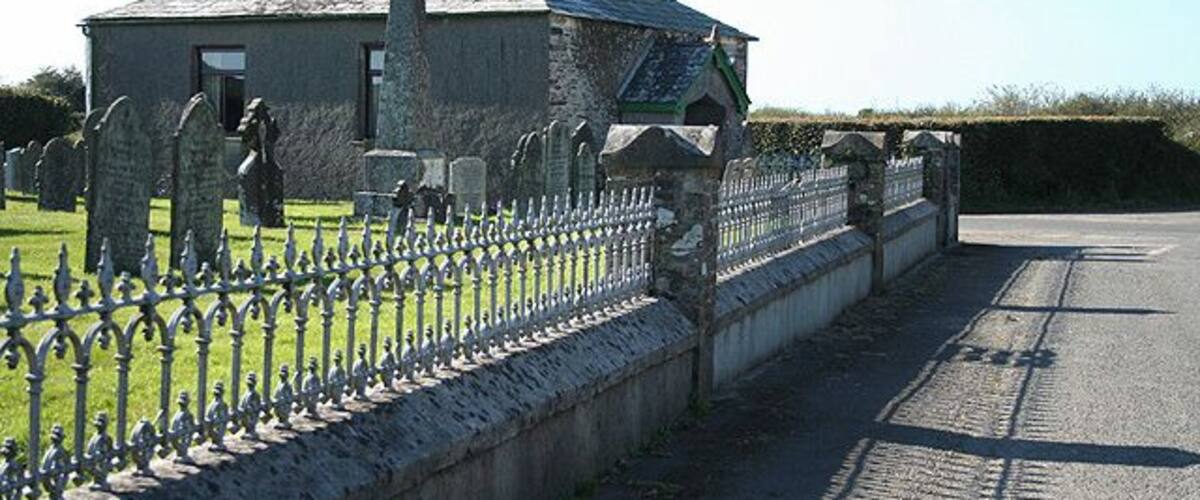 A cemetery with headstones, a stone building, and a metal fence.