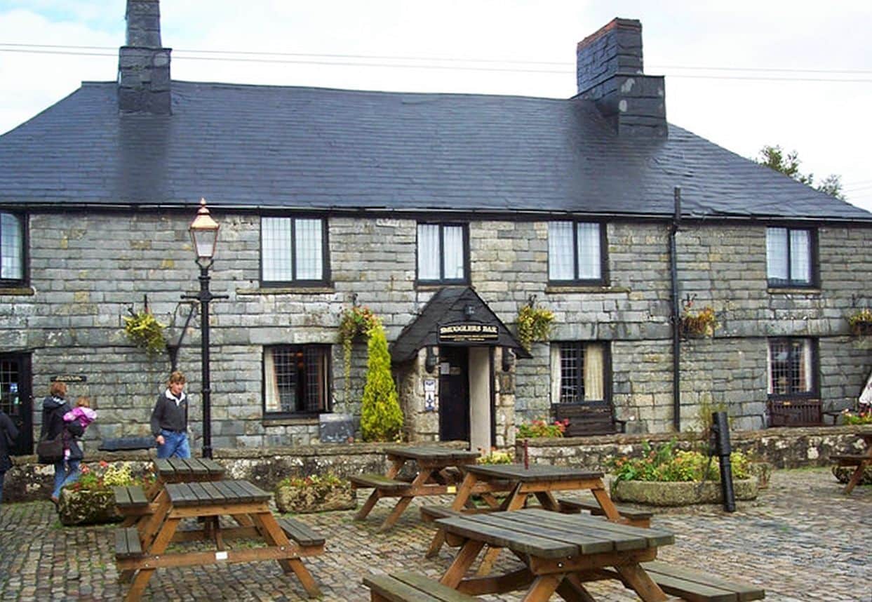 A stone building with a black awning labeled "The Blacksmith Bar" and outdoor wooden benches.