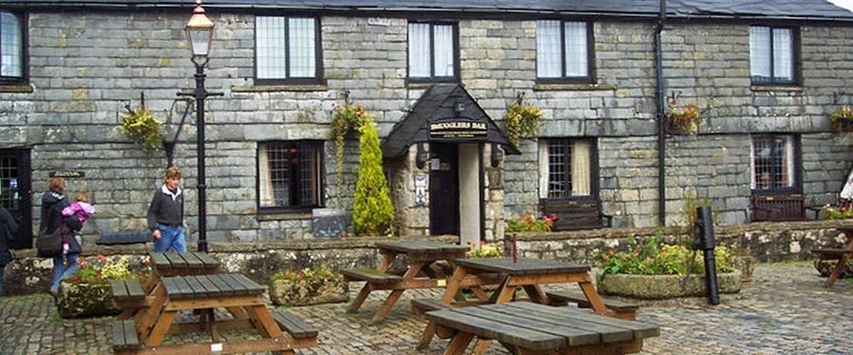 A stone building with a black awning labeled "The Blacksmith Bar" and outdoor wooden benches.