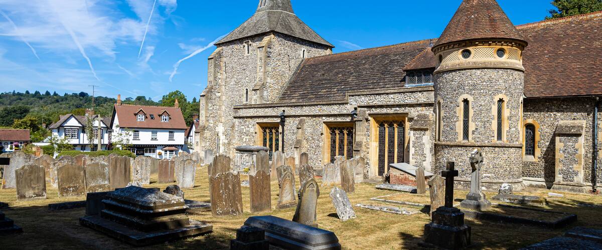 A historic church with two spires, a stone wall, and a cemetery with gravestones.