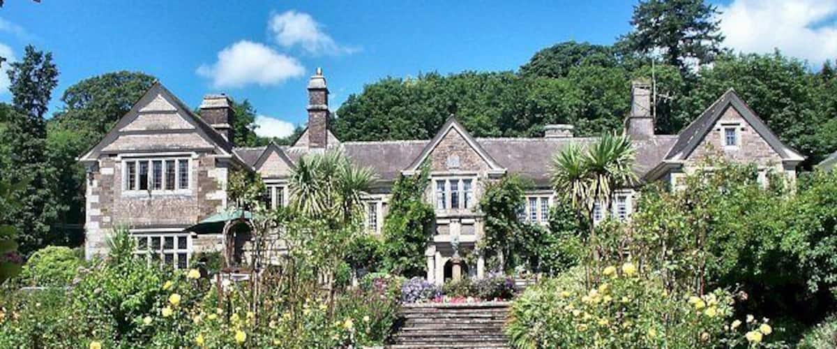 A large stone building with a symmetrical facade, a central staircase, and a well-maintained garden with various plants and flowers.