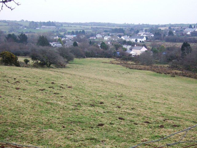 A rural landscape with a grassy field, scattered trees, and a distant village.