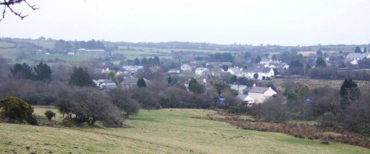 A rural landscape with a grassy field, scattered trees, and a distant village.