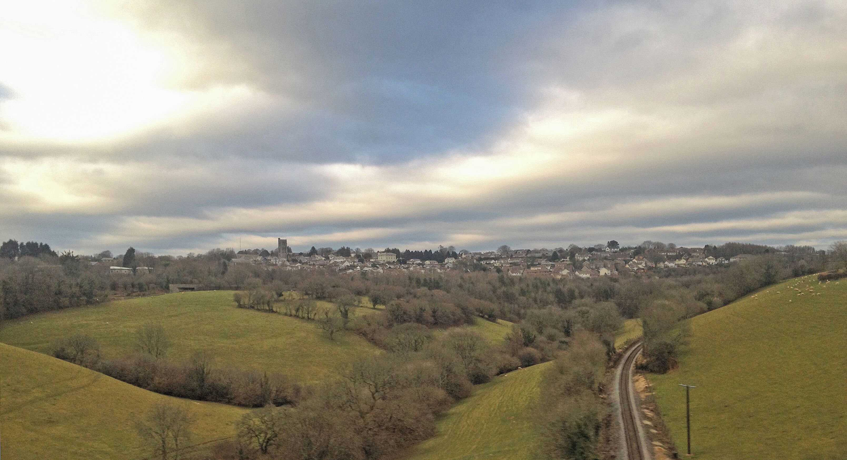 A rural landscape with rolling hills, a winding road, and a distant village with a prominent tower.