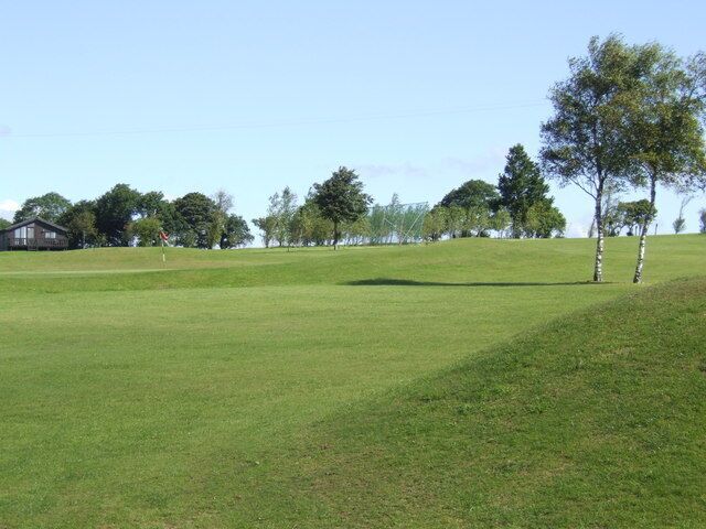A grassy field with a few trees and a building in the distance.
