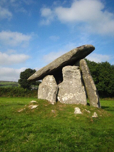 Una gran estructura de piedra vertical en un campo cubierto de hierba, con árboles al fondo.