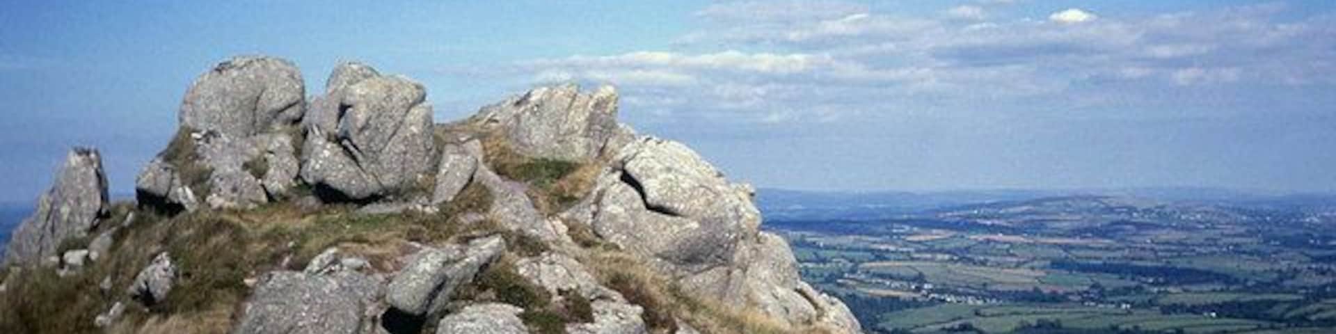 Summit of Sharptor Looking eastwards towards Dartmoor on the horizon. In the valley just to the right of the tor is the row of white cottages at Rilla Mill with the dome of Kit Hill beyond.