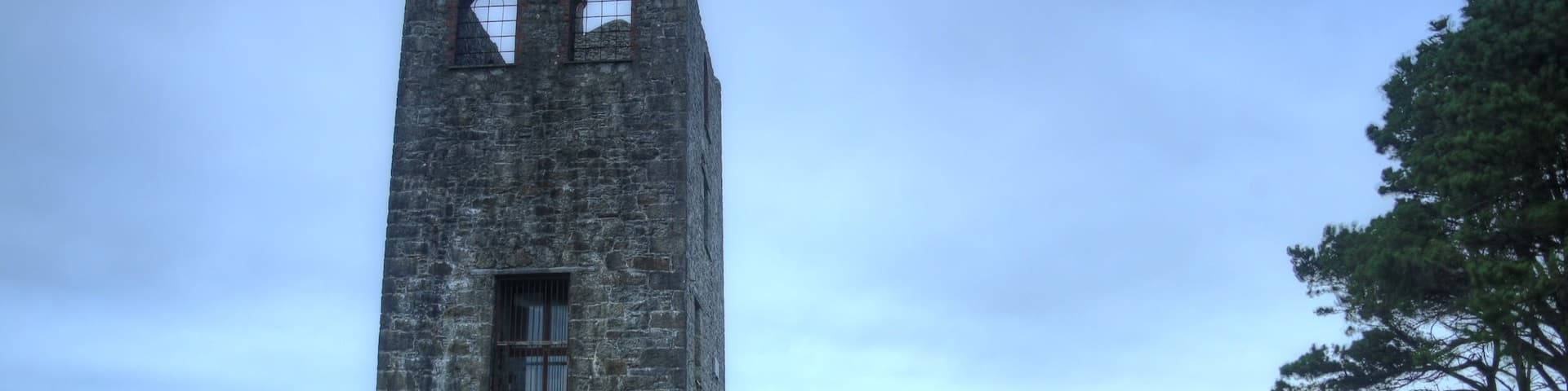 A tall stone tower with arched windows and a stone wall in a grassy field.