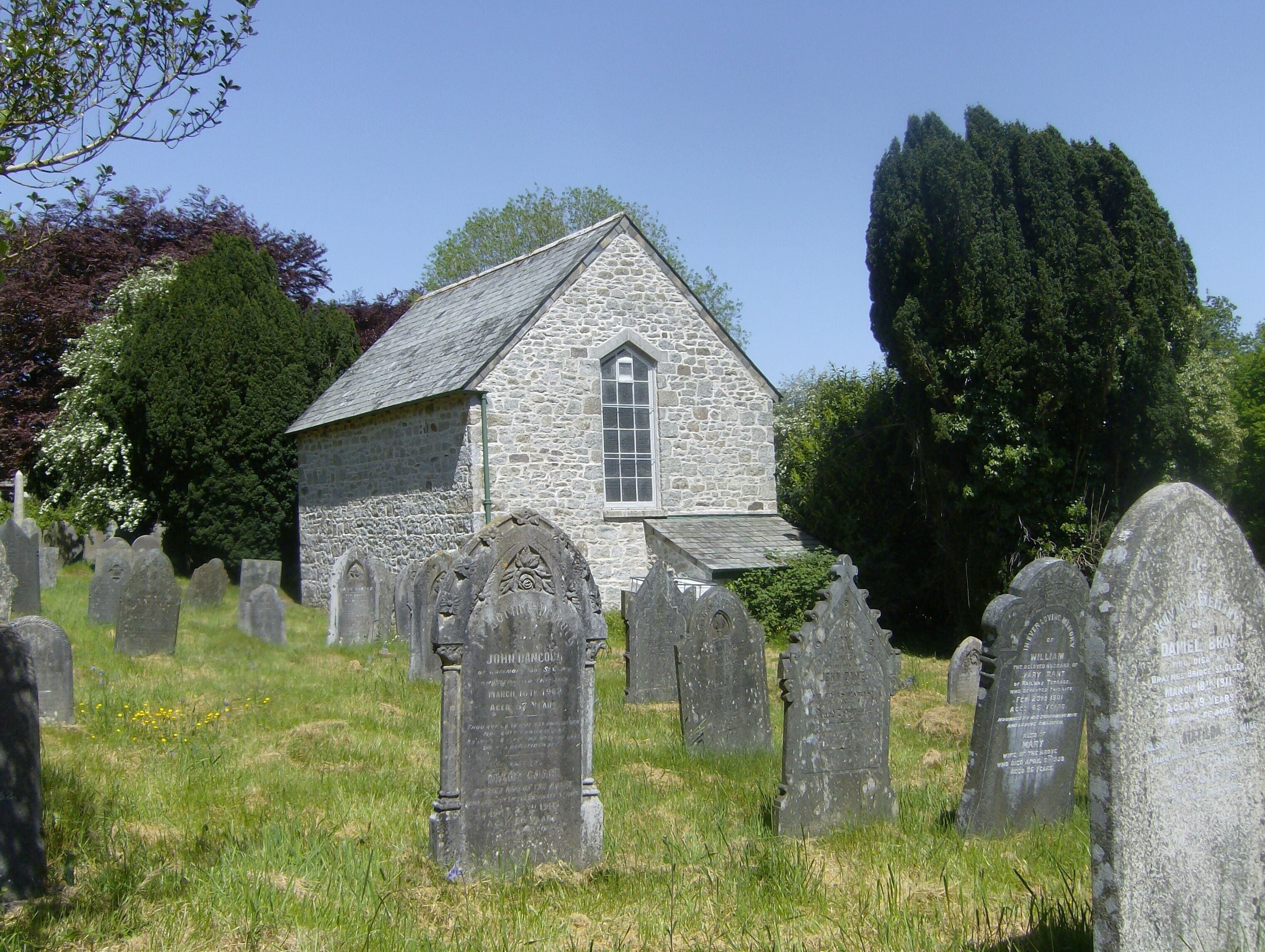 A stone church with a steeple, surrounded by a cemetery with numerous headstones.