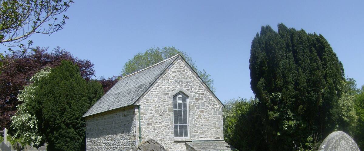 A stone church with a steeple, surrounded by a cemetery with numerous headstones.