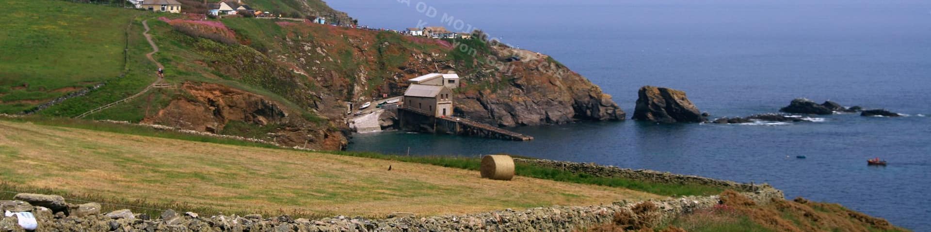 A coastal landscape with a lighthouse, a stone wall, and a grassy hill.