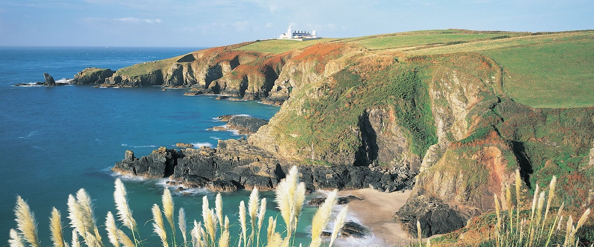 A coastal landscape with cliffs, a lighthouse, and a beach.