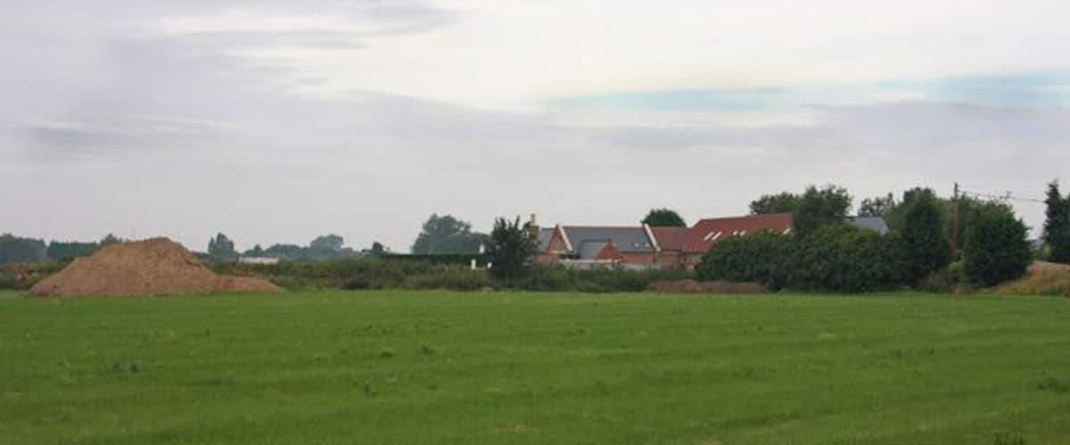 A green field with a pile of sand and a red-roofed building in the background.