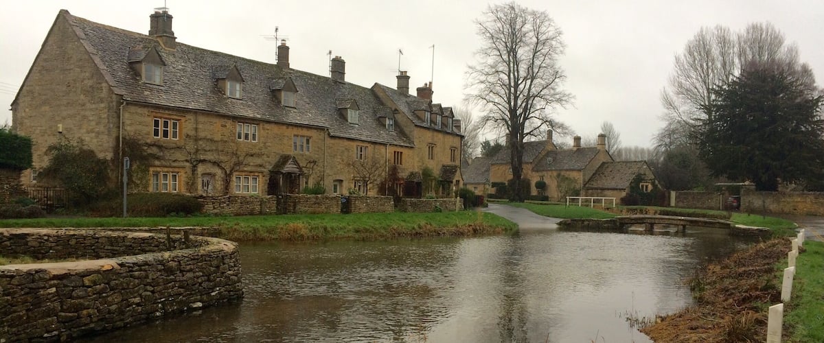 A stone bridge over a calm river, surrounded by traditional stone houses with sloped roofs.