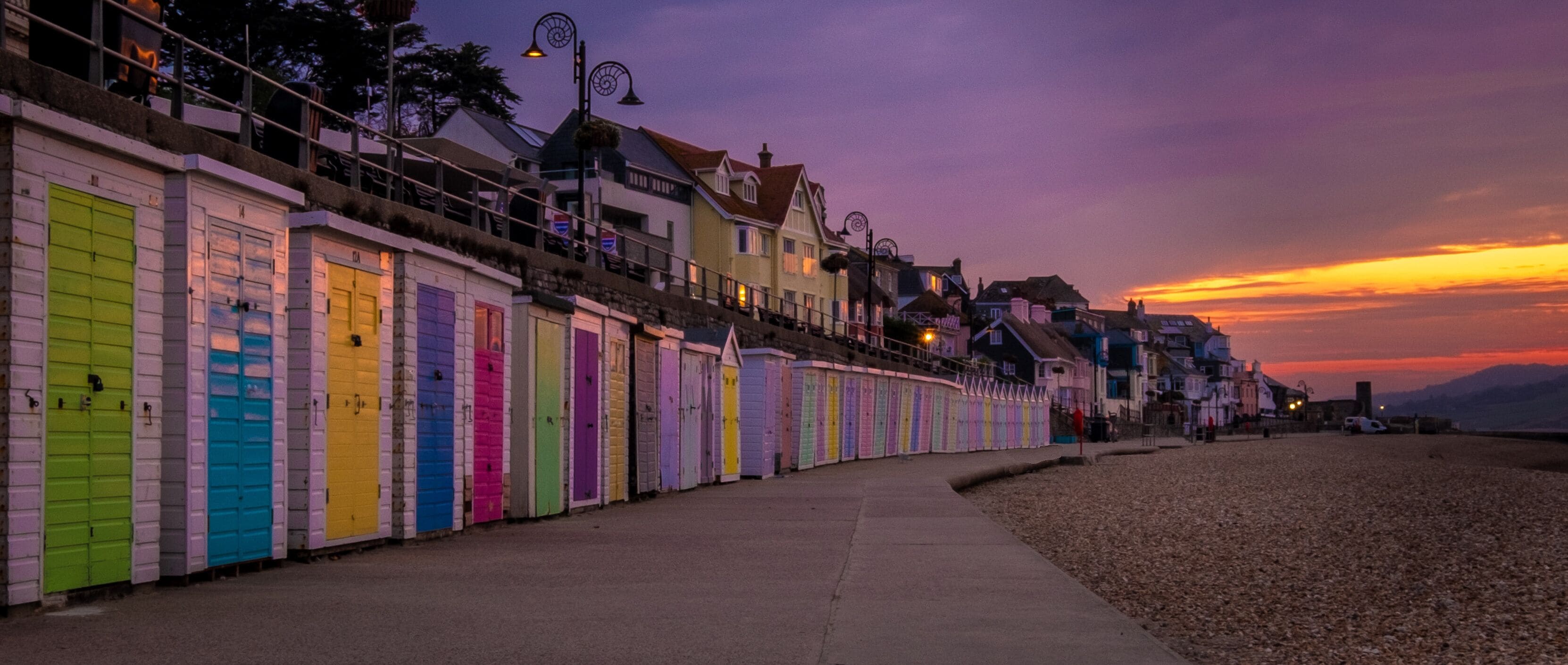 A row of colorful beach huts along a seaside promenade at sunset.