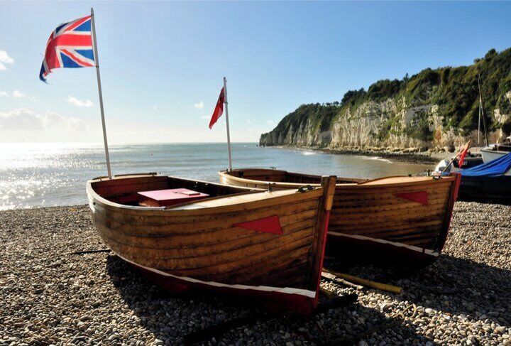 Two wooden boats with flags on a pebbled beach with cliffs in the background.