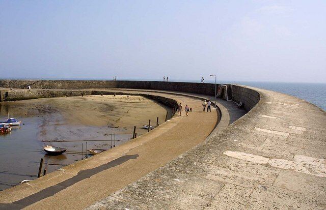 A curved concrete sea wall with a sandy beach and a small boat dock.