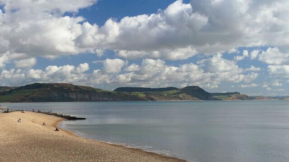 A beach with calm water, distant hills, and a partly cloudy sky.