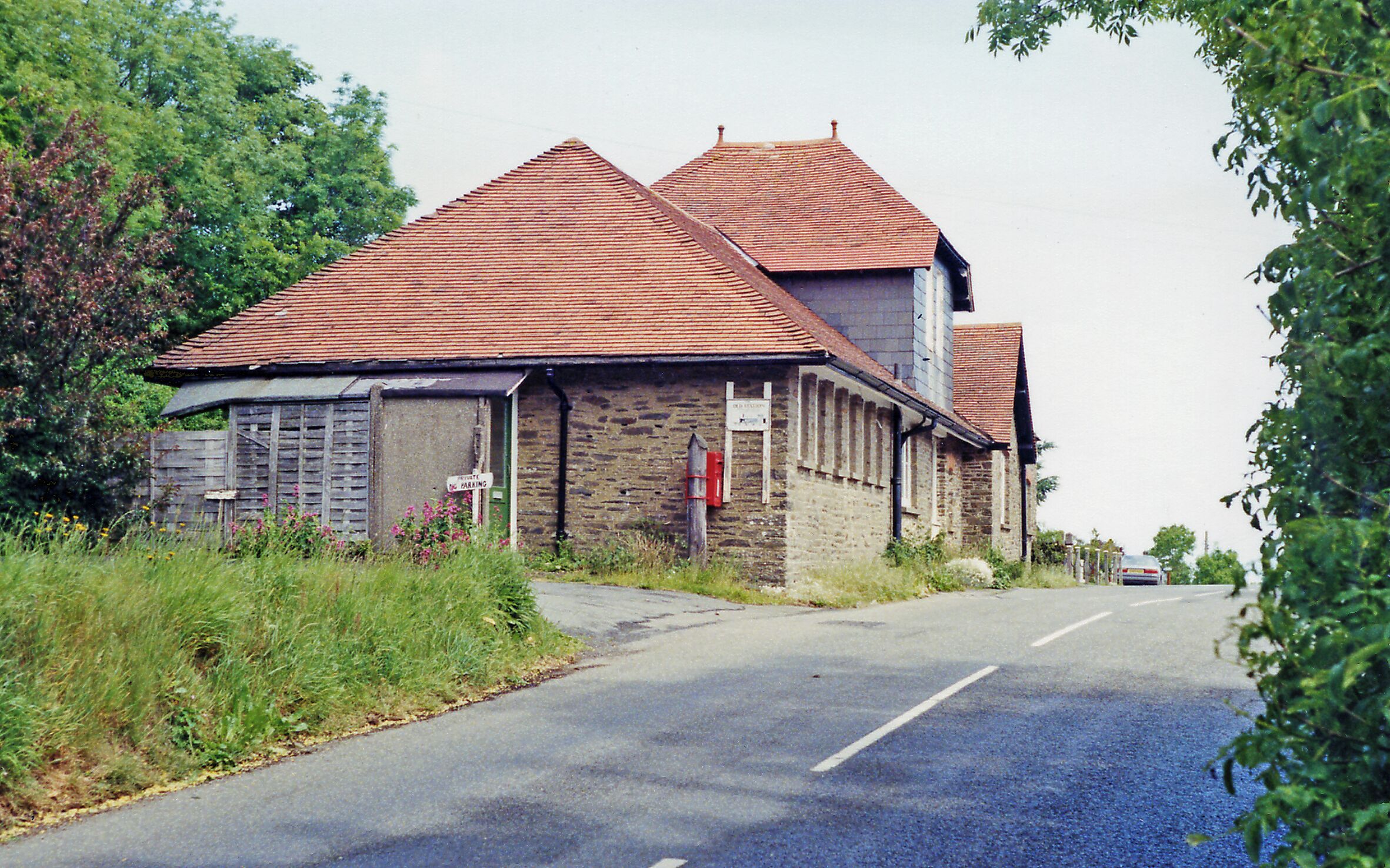 A rural road with a stone building with a red-tiled roof.