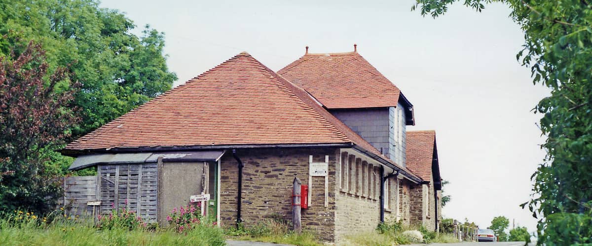 A rural road with a stone building with a red-tiled roof.