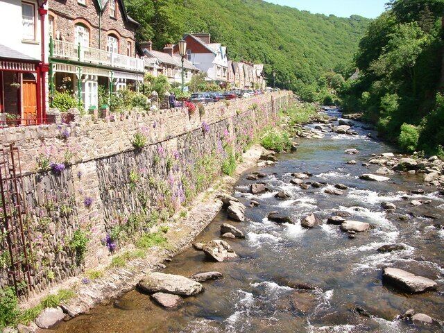 Un río con rocas, un muro de piedra con flores y edificios a lo largo de la orilla.
