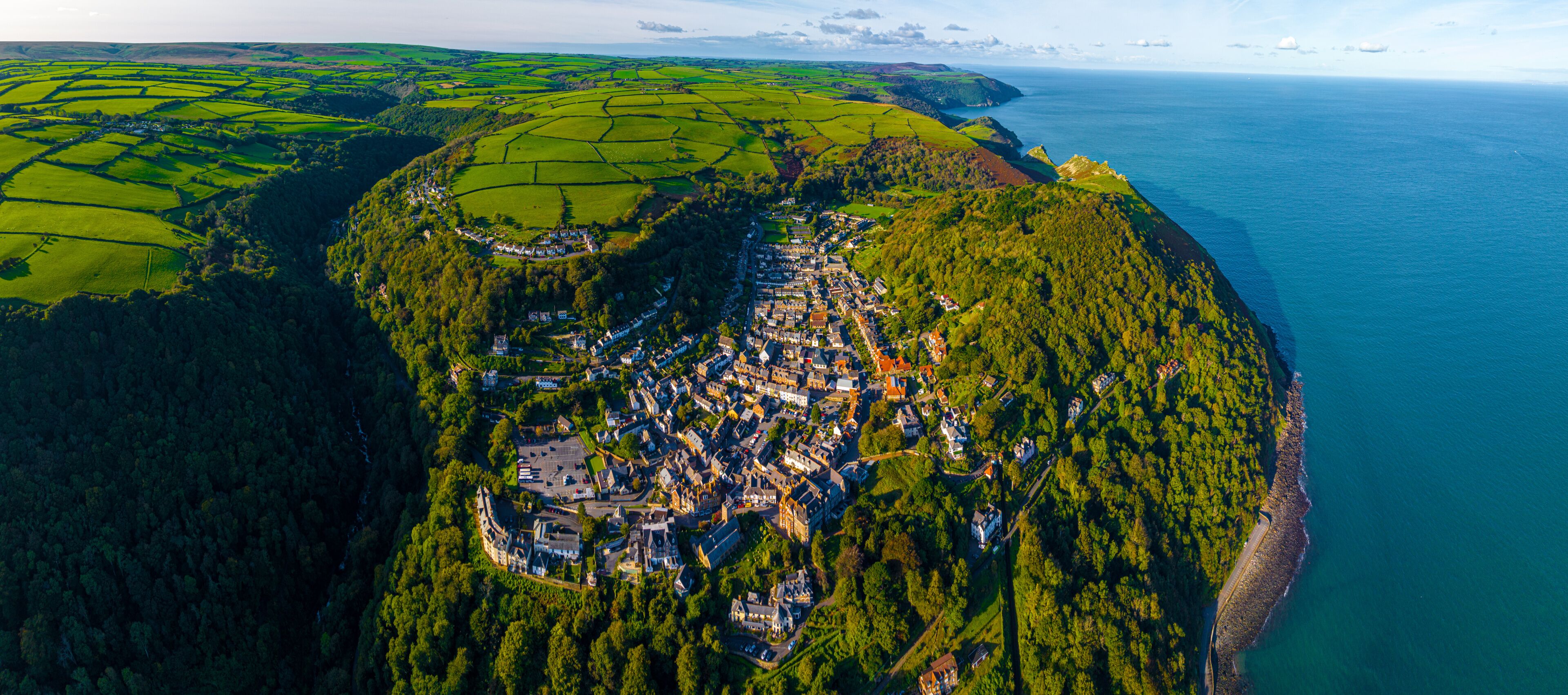 Vista aérea de un pueblo costero con un área boscosa densa, una costa despejada y un pequeño puerto.