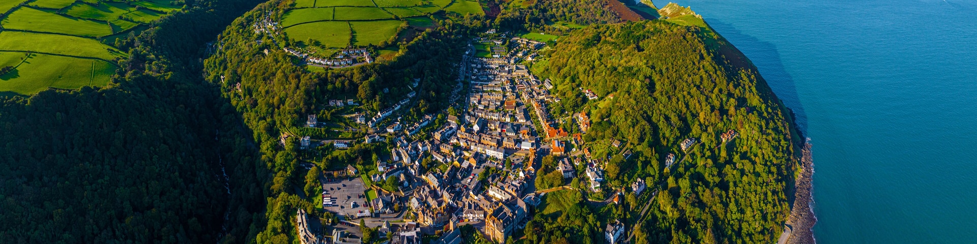 Vista aérea de un pueblo costero con un área boscosa densa, una costa despejada y un pequeño puerto.