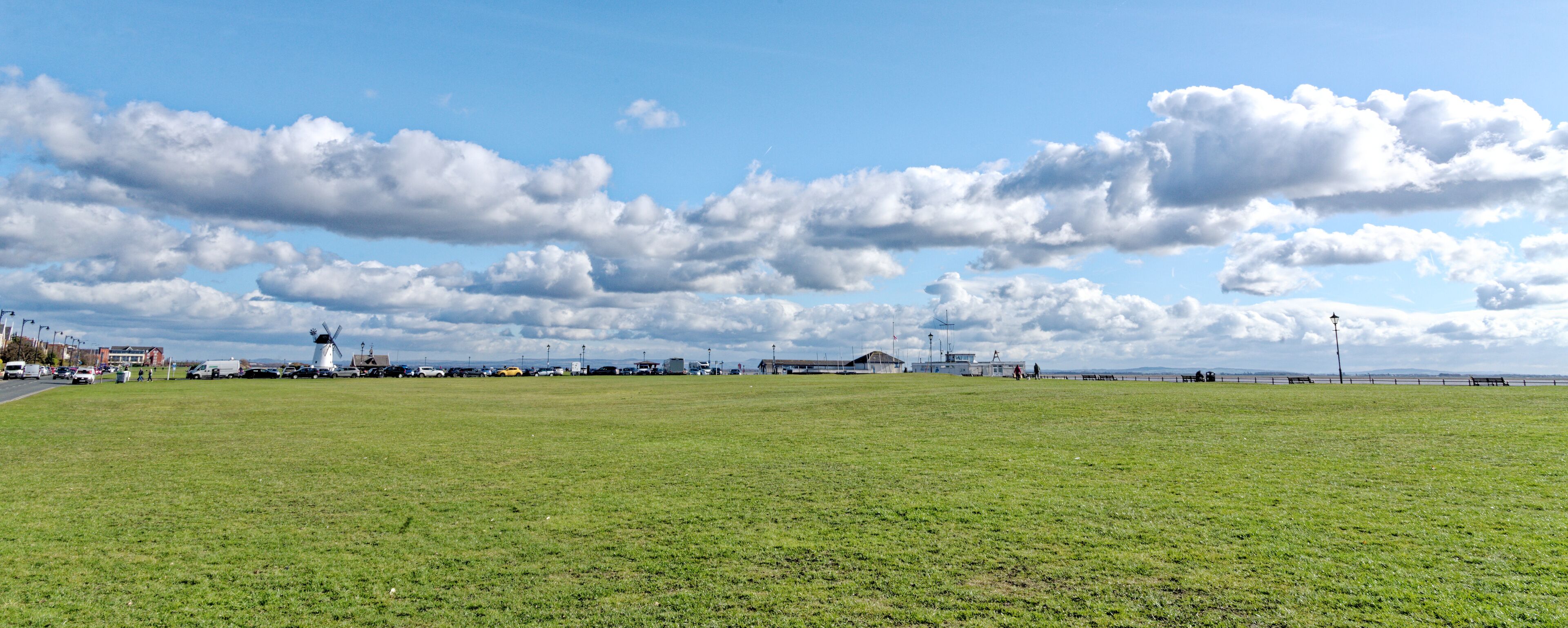 A grassy field with a windmill, buildings, and a distant shoreline.
