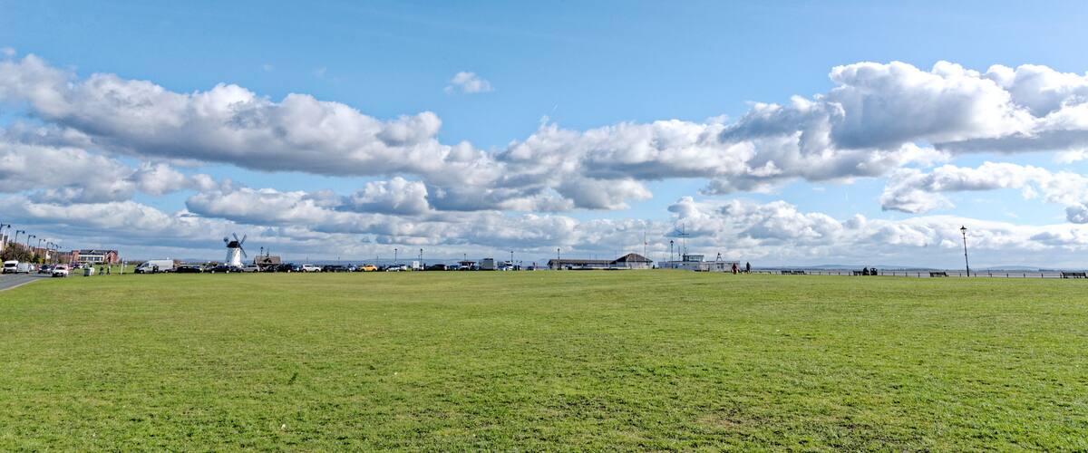 A grassy field with a windmill, buildings, and a distant shoreline.