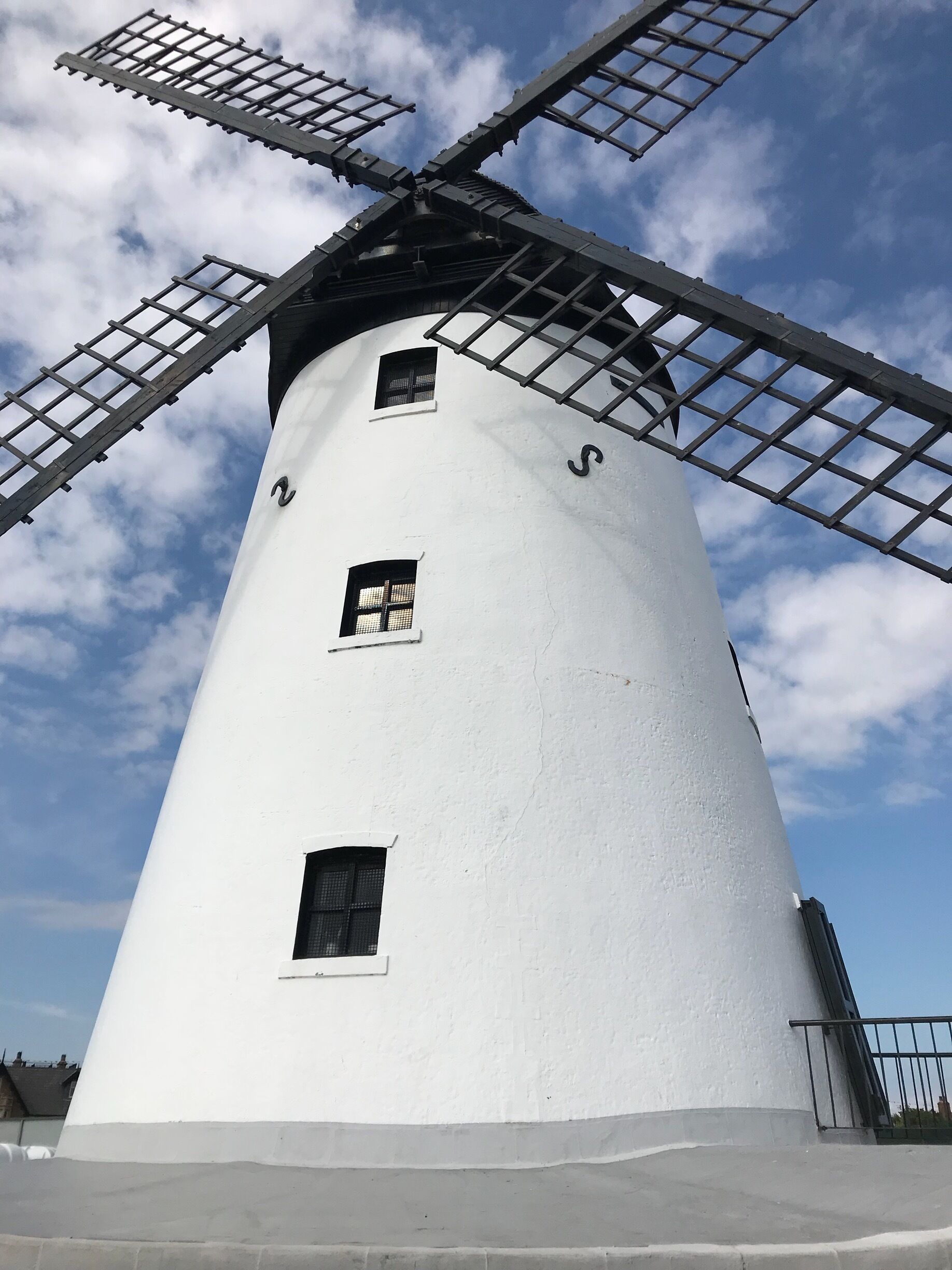 A white windmill with three windows and a metal lattice structure.