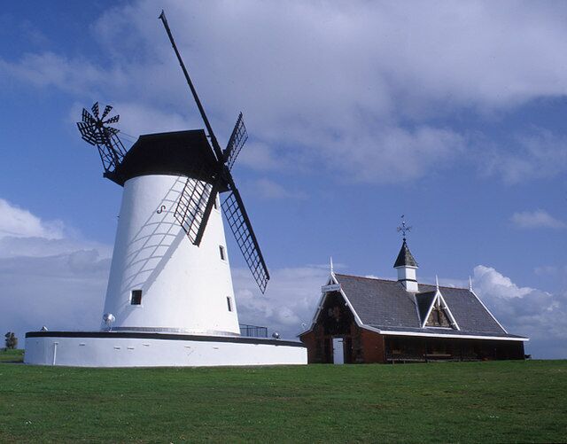 A white windmill with a black roof and a barn with a steep roof.