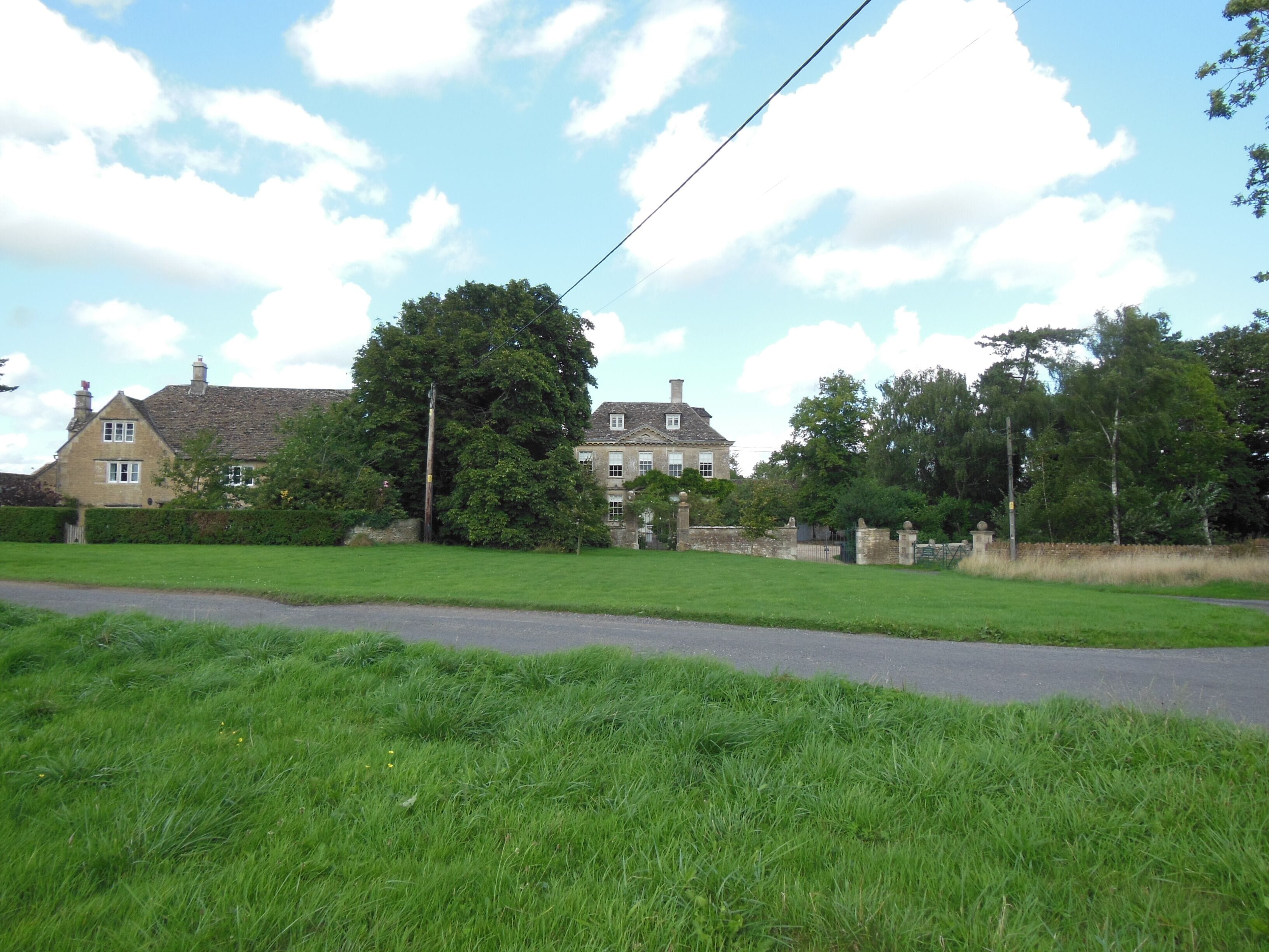 A rural landscape with a large house, green fields, and a clear sky.