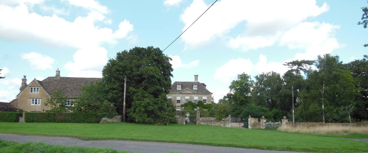 A rural landscape with a large house, green fields, and a clear sky.