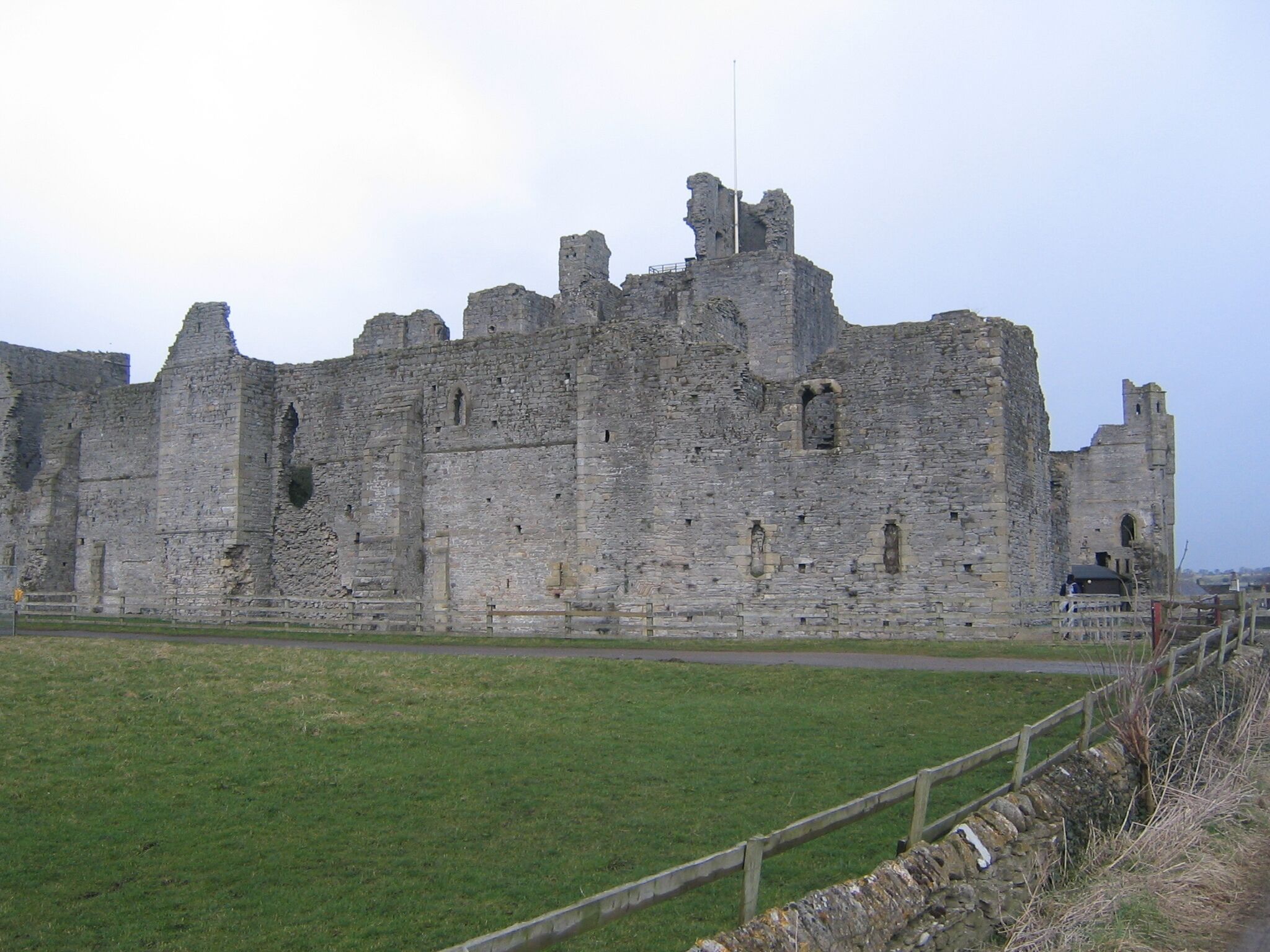 A historic stone castle with multiple towers and battlements, surrounded by a grassy field and a stone wall.