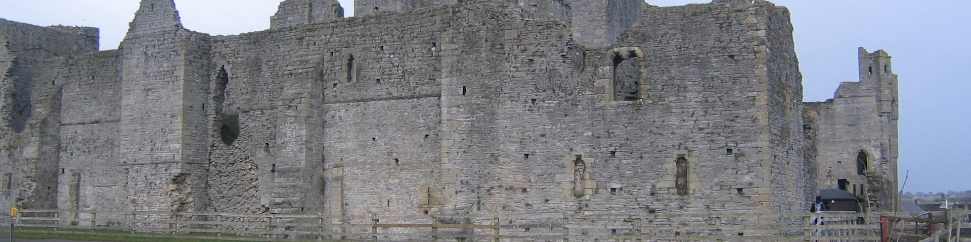 A historic stone castle with multiple towers and battlements, surrounded by a grassy field and a stone wall.