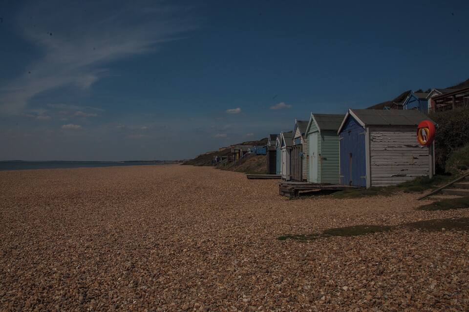 A pebbled beach with wooden beach huts and a clear blue sky.