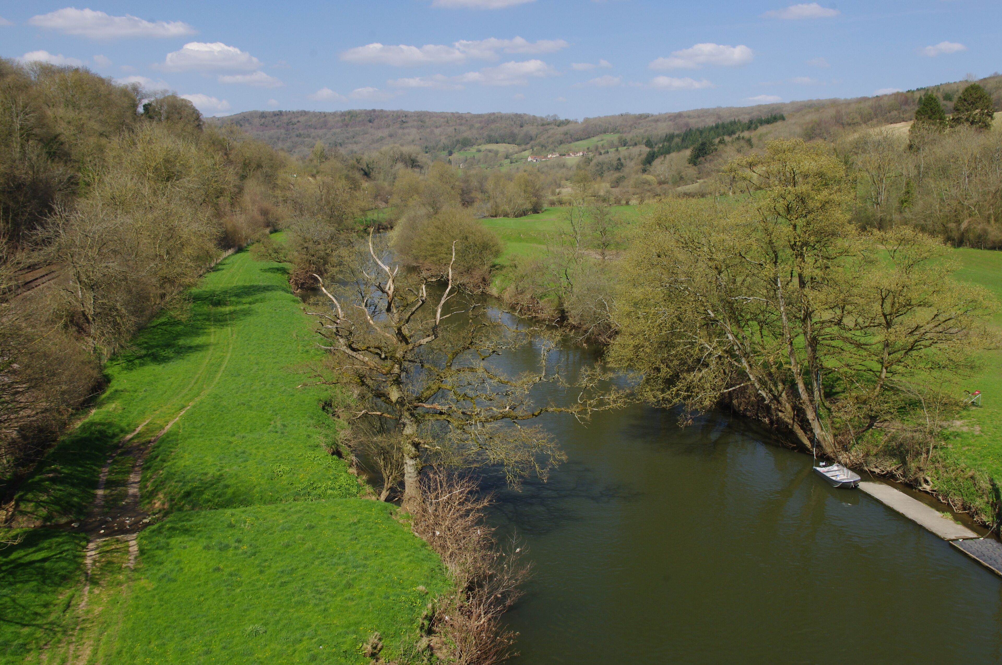 A river flowing through a green valley with trees and hills in the background.